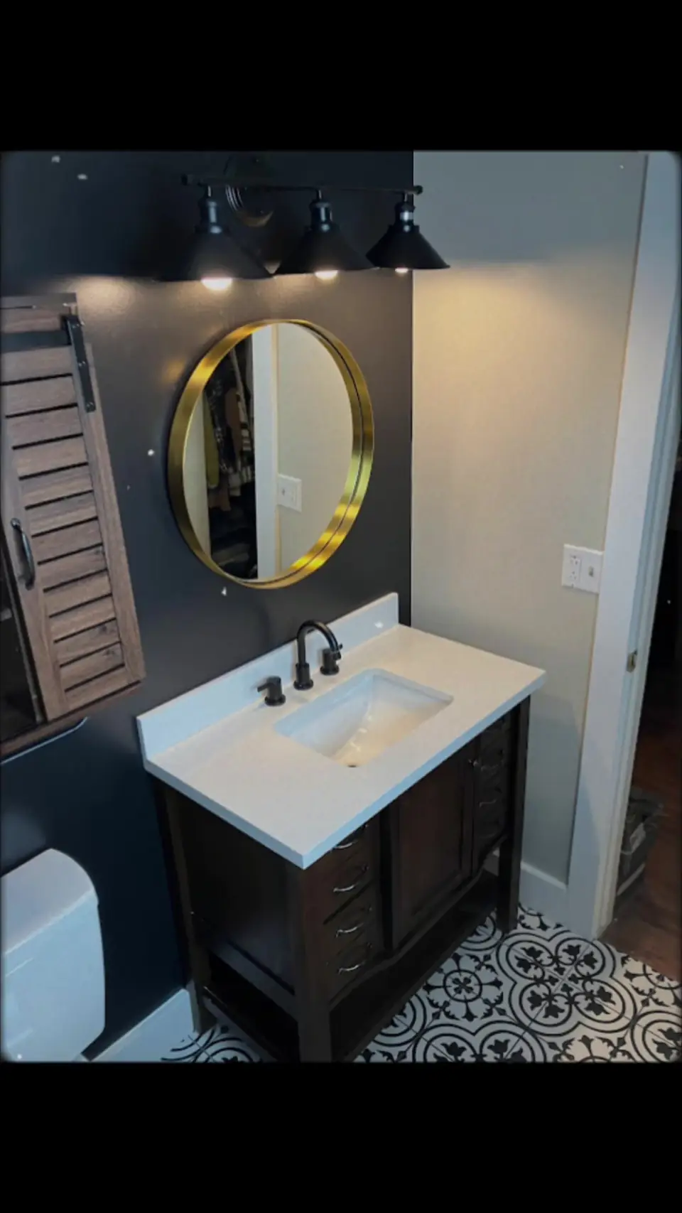 Luxury bathroom with black vanity, white countertop, gold circular mirror, and patterned floor