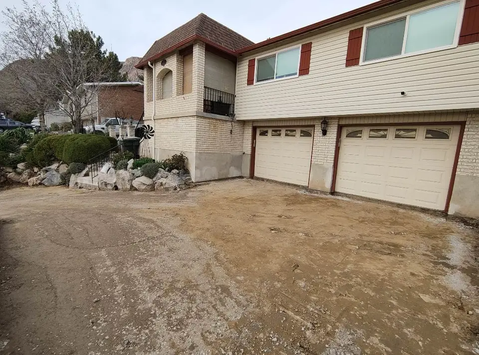 Dirt and gravel driveway base in front of a house with red shutters