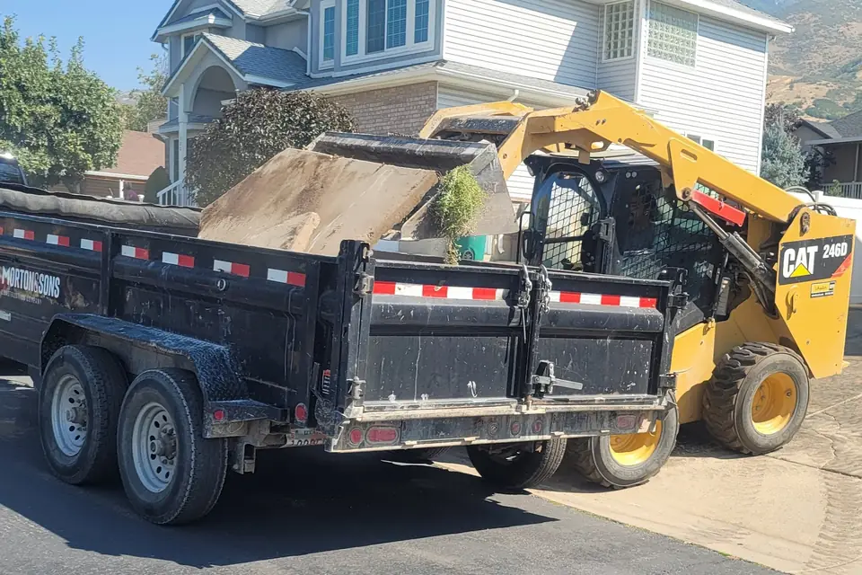 Skid steer loading dirt into a dump trailer at a house