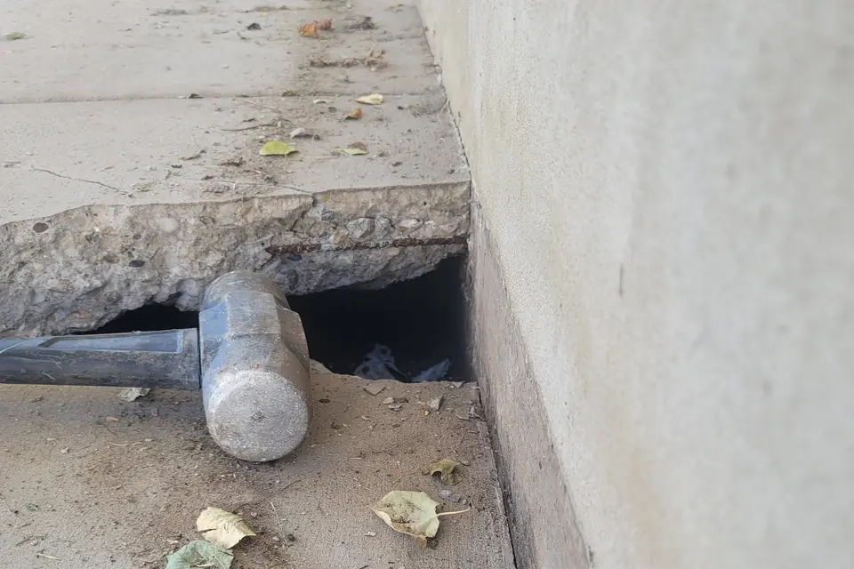 Void under a broken concrete slab edge with a sledgehammer for scale